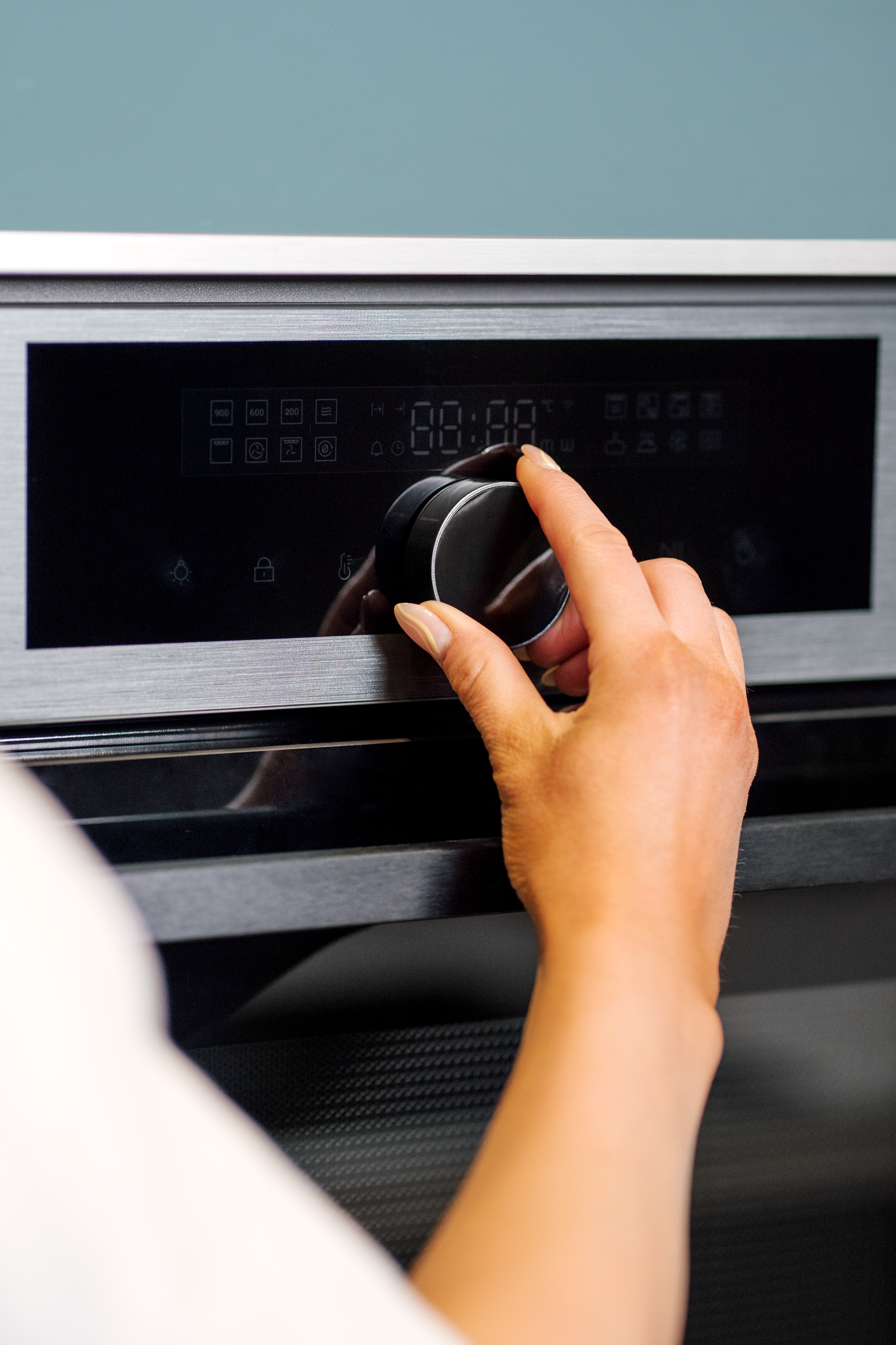A person adjusts the dial on an oven with a digital display.